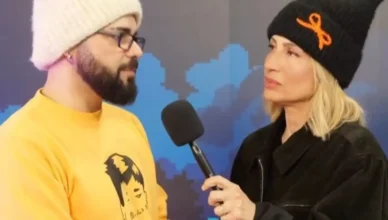 Ο τραγουδιστής Ακύλας φοράει το χαρακτηριστικό του σκουφάκι και χαμογελά κατά τη διάρκεια συνέντευξης για τη Eurovision 2026.